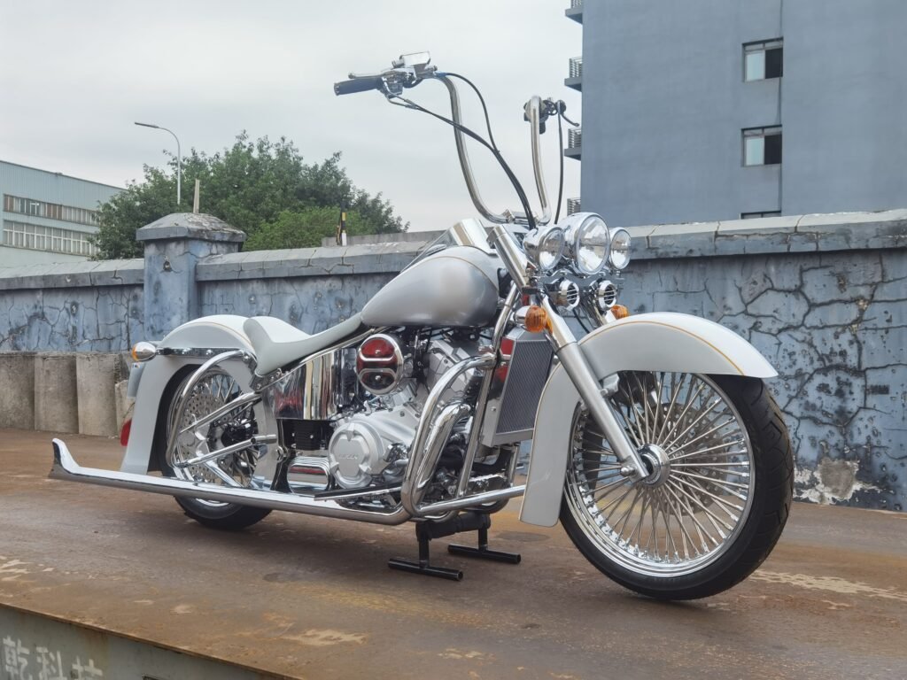 White custom cruiser motorcycle build with triple headlights, ape hanger handlebars and spoke wheels in front three quarter view