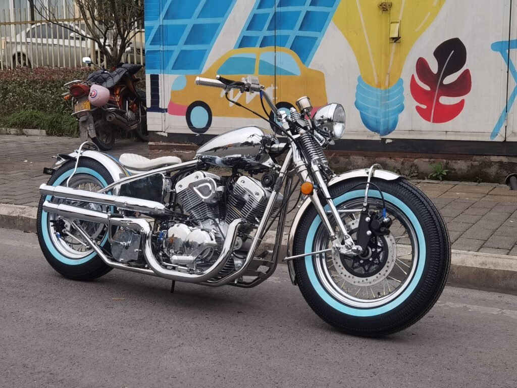Chrome custom bobber motorcycle with light blue whitewall tires, solo seat and spoke wheels in front three quarter street view