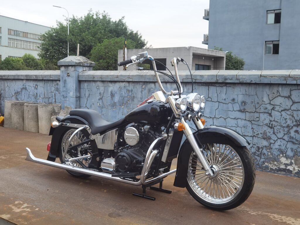 Black custom cruiser motorcycle build with triple headlights, high handlebars, chrome exhaust and front spoke wheel in front three quarter view