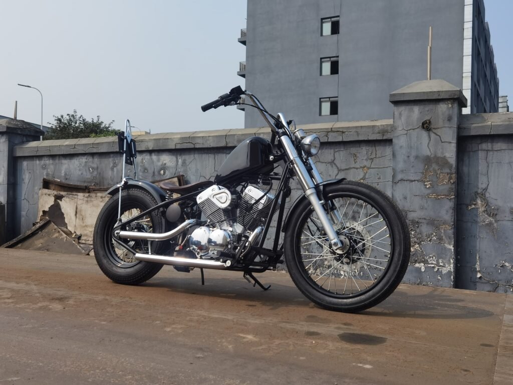 Minimalist black bobber motorcycle build with ape hanger handlebars, solo seat, spoke wheels and chrome V twin engine in front side view